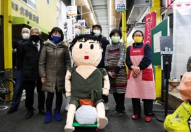 「みのる坊」人形を囲んで笑顔をみせる大日六商店街の店主ら＝神戸市中央区大日通６