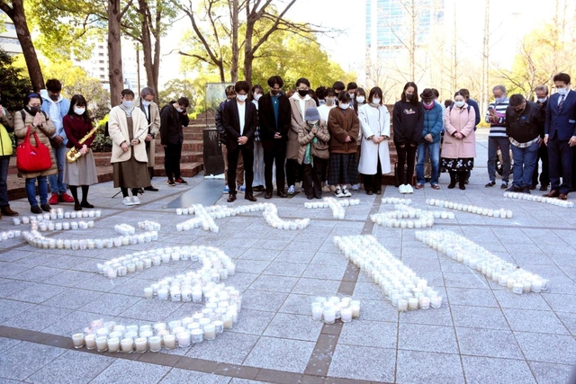 並べたキャンドルの前で、東日本大震災の犠牲者に黙とうをささげる人々＝神戸市中央区加納町６