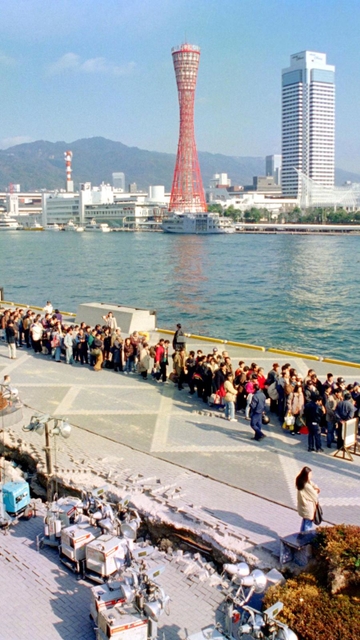 損傷した高浜岸壁で、大阪行きのフェリーを待つ人たちの後ろにそびえる＝１９９５年１月２０日
