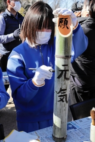 切った竹に筆で文字を書き入れる生徒＝神戸市北区山田町藍那、あいな里山公園