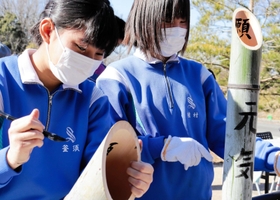 切った竹に筆で文字を書き入れる生徒たち＝神戸市北区山田町藍那、あいな里山公園