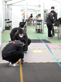 大規模接種会場の動線を示すテープを床に貼るスタッフら＝神戸市兵庫区御崎町１、ノエビアスタジアム神戸