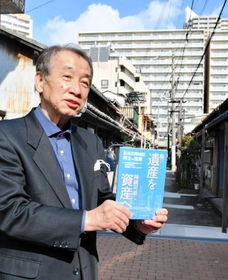 再開発ビルを背に、新長田駅南地区再開発事業の検証報告書について説明する出口俊一さん＝神戸市長田区久保町７