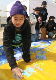 友人や通行人に協力してもらい、ウクライナ国旗をイメージした絵を制作する小野万葉さん＝メリケンパーク