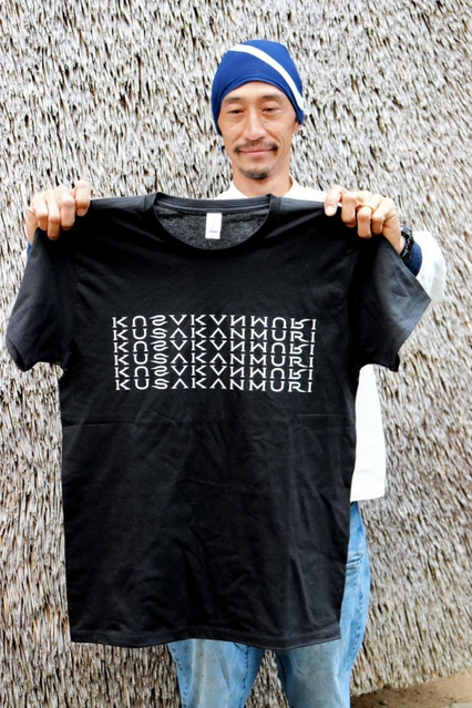 かやぶきを使った壁の前でＴシャツを手にする相良育弥さん＝神戸市北区淡河町