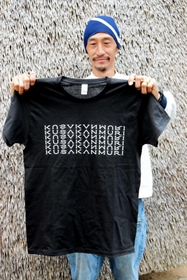 かやぶきを使った壁の前でＴシャツを手にする相良育弥さん＝神戸市北区淡河町