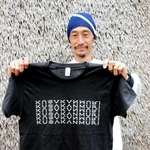 かやぶきを使った壁の前でＴシャツを手にする相良育弥さん＝神戸市北区淡河町