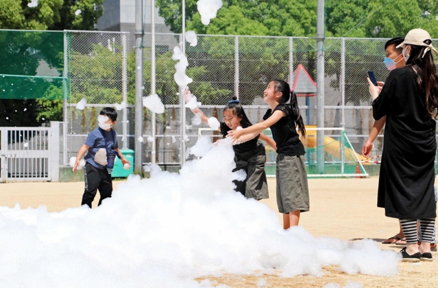 機械で降らせた「消えにくい泡」を触って遊ぶ児童たち＝神戸市中央区吾妻通４