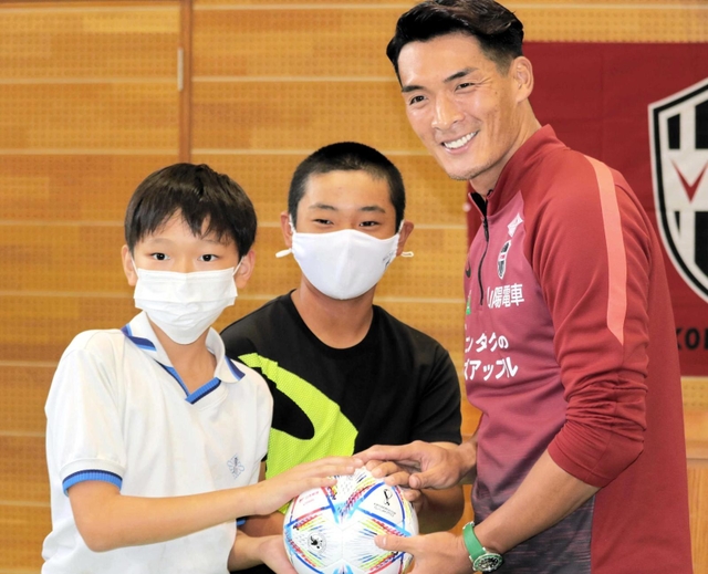 贈ったボールを手に児童らと記念写真に納まる槙野智章選手（右）＝宮川小学校
