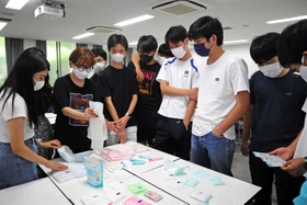 多種類の生理用品が並ぶ。「買ってきてと言われたらどれがいいのかな」と、灘高生に問いかける甲南女子大生＝神戸市東灘区、灘高校