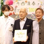 安井久晃医師（左）から色紙を受け取った寺西清春さんと妻の久美子さん＝神戸市立医療センター中央市民病院