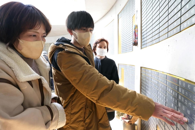 母、祖母と一緒に亡き祖父の名を確かめる松端泰久さん（中央）＝１７日午前１１時２１分、中央区加納町６