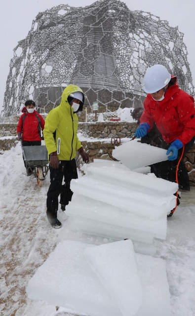 雪が降りしきる中、氷棚でできた天然の氷を切り出す職員ら＝２７日午前、神戸市灘区六甲山町、自然体感展望台「六甲枝垂れ」