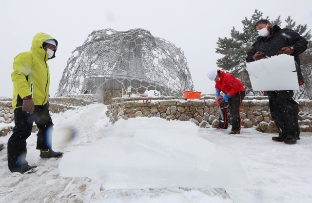 雪が降りしきる中、氷棚でできた天然の氷を切り出す職員ら＝２７日午前、神戸市灘区六甲山町、自然体感展望台「六甲枝垂れ」