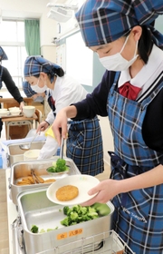 神戸タータン柄のエプロンを着て給食を皿に盛る生徒たち＝神戸市北区八多町