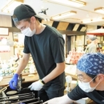 炭酸せんべいを焼くマリー・ダニエルさんと、火加減を調整する平野屋本舗の平野雅之社長＝神戸市北区有馬町