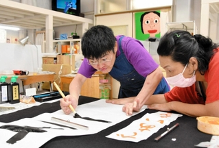 スタッフとともに書道に取り組む佐田かおりさん（左）。勢いのある筆運びが作品に生きる＝神戸市長田区川西通５