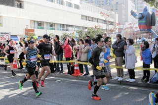 鉄人２８号のモニュメント前を走り抜けるランナーに声援を送る人たち＝１９日午前、長田区若松町６