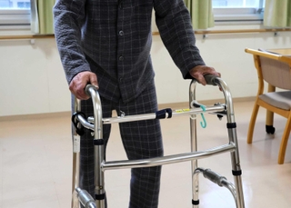 歩行器を使って歩く男性。火災後、歩けるようになるまで５カ月かかった＝神戸市長田区