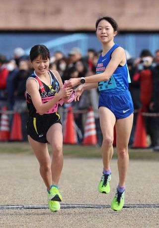 女子・西区の２区池野絵莉選手（右）からたすきを受ける３区池野芹梨選手＝加古川市の加古川河川敷マラソンコース（撮影・笠原次郎）