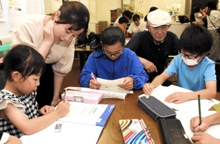 放課後に集まり、宿題に取り組む子どもたち。学生ボランティアや中村保佑さん（右から２人目）が見守る＝神戸市東灘区甲南町２