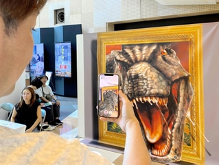 スマホの専用アプリで、絵の恐竜が飛び出して見えるトリックアートを楽しむ来場者＝神戸市中央区東川崎町１、カルメニ