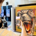 スマホの専用アプリで、絵の恐竜が飛び出して見えるトリックアートを楽しむ来場者＝神戸市中央区東川崎町１、カルメニ