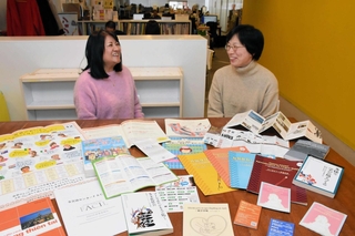 生活情報を多言語で翻訳した発行物などを前に、歩みを語る吉富志津代特別顧問（左）と李裕美理事長＝神戸市長田区海運町３