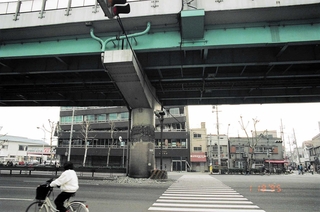 コンクリートが剝がれて曲がった鉄骨がむき出しになった阪神高速神戸線の橋脚と、３階部分がつぶれたビル＝１９９５年１月１８日（和田幹司さん撮影、神戸アーカイブ写真館提供）