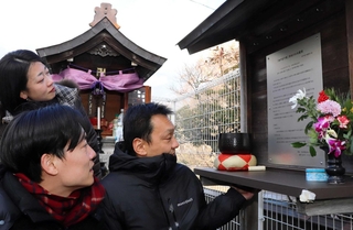 奥にあるほこらの前に設置された銘板。神戸母子寮で母を亡くした鈴木佑一さん（手前左）らが万感の表情で見つめた＝神戸市兵庫区湊川町１０