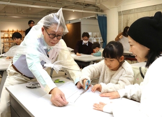 ごみ袋を使ったポンチョの工作に挑戦する親子と久保田雅人さん（手前左）＝神戸市中央区小野浜町