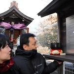 奥にあるほこらの前に設置された銘板。神戸母子寮で母を亡くした鈴木佑一さん（手前左）らが万感の表情で見つめた＝神戸市兵庫区湊川町１０