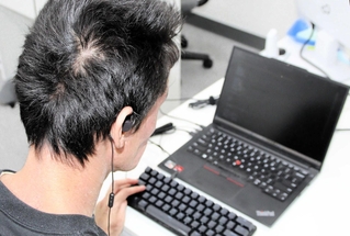 全盲のため、イヤホンで音声を確認しながらパソコンを操作するＩＴエンジニアの氏家猛さん＝神戸市中央区琴ノ緒町５