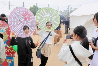 マンホール形のかぶりものを頭に着けて写真を撮る子どもたち＝住吉公園グラウンド