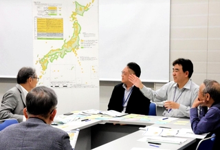 資源エネルギー庁や原子力発電環境整備機構の担当者（右奥）から説明を受ける参加者＝中央区港島中町６、神戸国際会議場