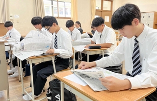 朝刊を開いて目を通す生徒＝啓明学院高校