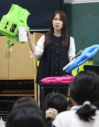 ライフジャケットを手に水難事故の恐ろしさを強調する岡真裕美さん＝西郷小学校