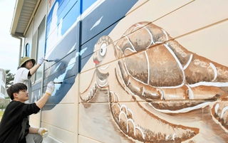 須磨海岸のプレハブ外壁に描かれた絵を塗り直す関西国際大の学生ら＝須磨区須磨浦通４