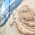 須磨海岸のプレハブ外壁に描かれた絵を塗り直す関西国際大の学生ら＝須磨区須磨浦通４