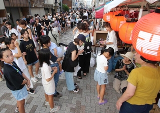 地蔵の前で手を合わせ、菓子を受け取る子どもたち。親子連れらが長い列を作った＝長田区庄田町３