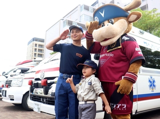 ヴィッセル神戸のマスコット「モーヴィ」と一緒に救急車両の前で記念写真に納まる子どもら＝ノエビアスタジアム神戸