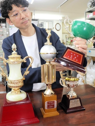 寄付予定のトロフィーを手に「どんな形のものでも大歓迎」と呼びかける藤井淳史社長＝毛利マーク
