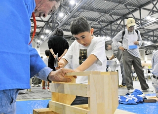 職人にアドバイスをもらいながら金づちを持って本棚づくりに挑戦する子ども＝神戸国際展示場