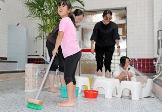 浴場の床や椅子を清掃する親子連れ＝神戸市長田区の本庄湯