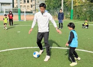 コーチの江口倫司さん（中央）から、サッカーのプレーの基本を教わる親子＝神戸リガッタ・アンド・アスレチック倶楽部