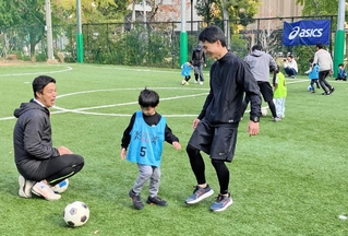 コーチの江口倫司さん（左）からプレーの基本を教わる親子＝神戸リガッタ・アンド・アスレチック倶楽部