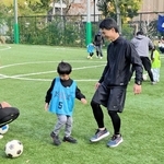 コーチの江口倫司さん（左）からプレーの基本を教わる親子＝神戸リガッタ・アンド・アスレチック倶楽部