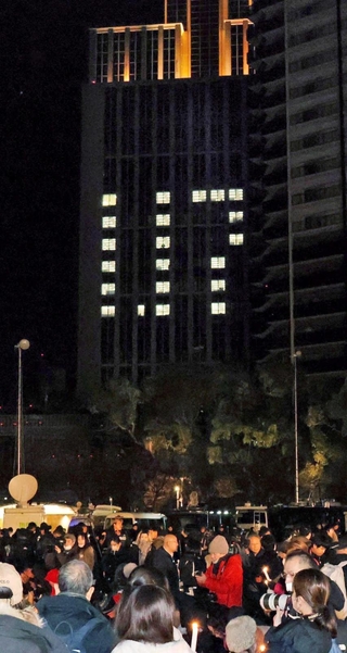 竹灯籠に手を合わせる人たちを、ビルの「１．１７」が見守る＝１月１７日午前５時１０分、東遊園地