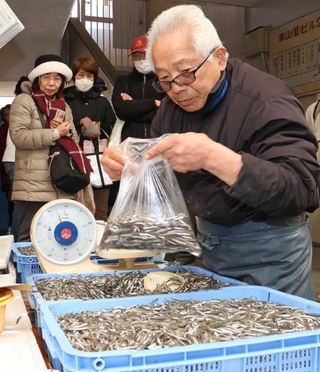 シンコを袋詰めする鶴谷伸之さん（手前）。旬の味覚を求める買い物客が列をつくって待っていた＝明石屋丸徳