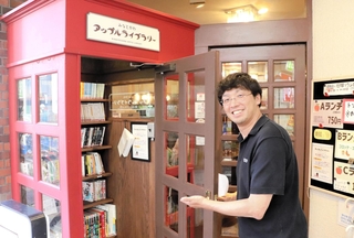 電話ボックス風のミニ図書館を紹介する岡部亮司さん＝喫茶アップルハウス